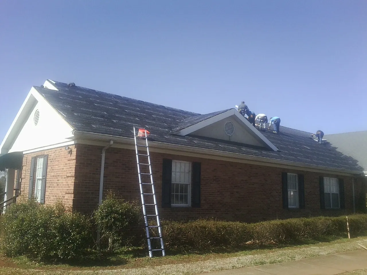 Crew tearing shingles off a brick ranch roof with a ladder set — Metal Roof Repair work by our crew in Doon
