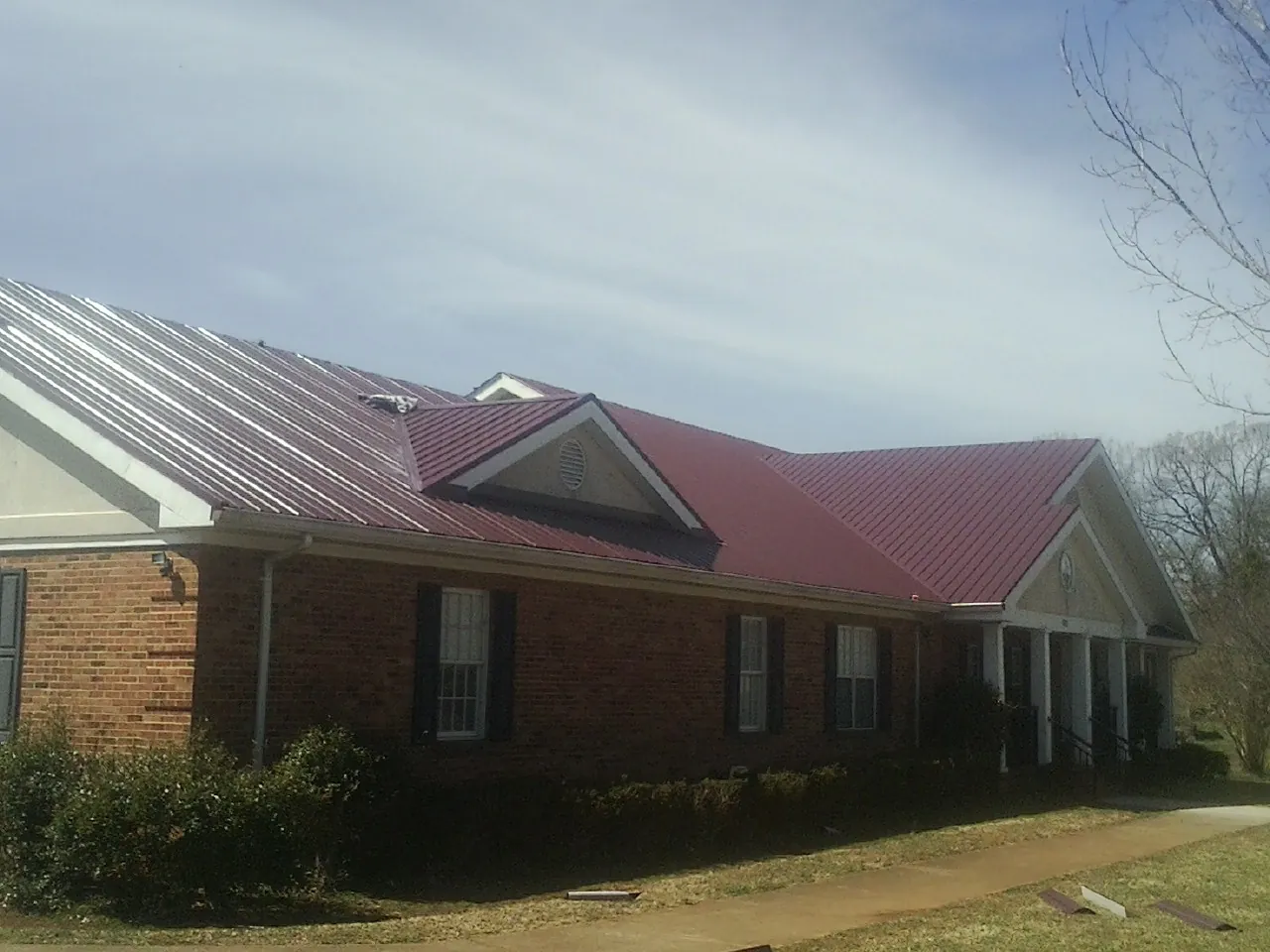 Red metal roof with gabled entries on a long brick building, from a Hail Damage Roof Repair job in Doon
