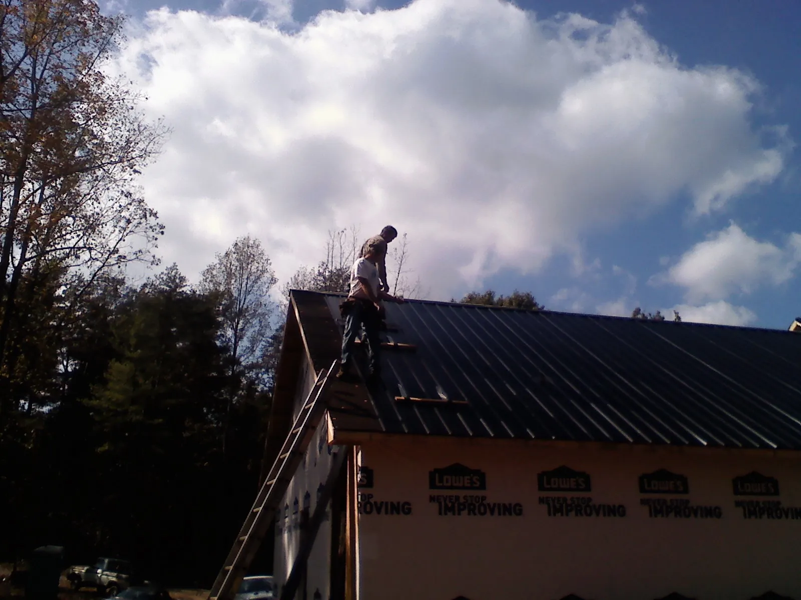 Roofer fastening dark metal panels high against a cloudy sky, from a Roof Inspection job in Doon