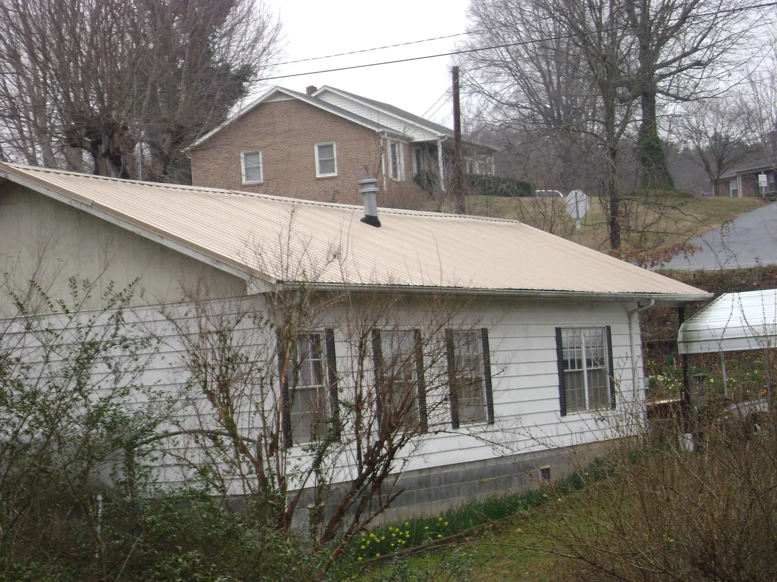 Tan metal roof on a white sided house set into a hillside — Commercial Roofing by Roofing Brothers in Doon