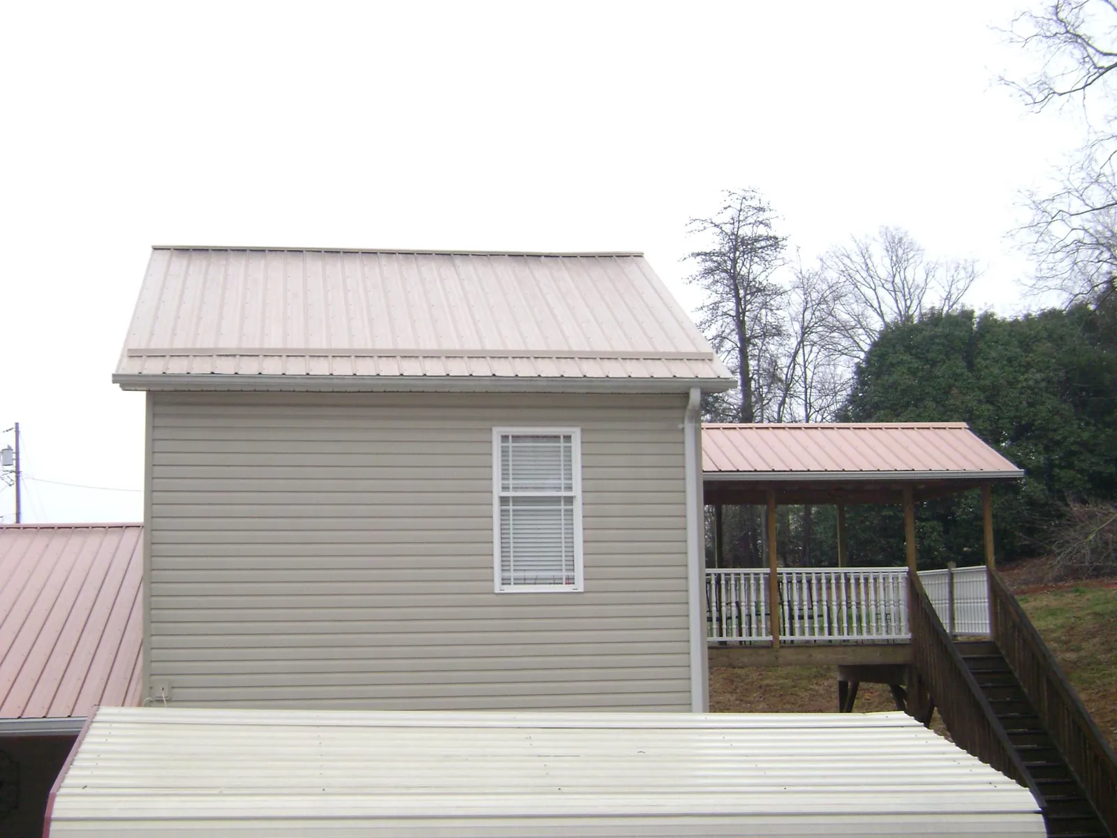 Tan metal roofs on a two story addition and attached porch, from a Roof Replacement job in Doon
